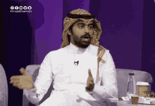 a man in a white shirt and a head scarf is sitting on a couch and talking
