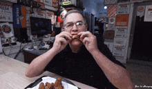 a man is eating chicken wings in front of a wall that says ' maury 's pizza '