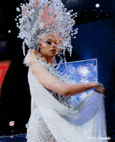a woman in a white dress and a silver headpiece is dancing on a stage with a tumblr logo in the corner