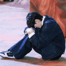 a young man is sitting on the floor with his head down .