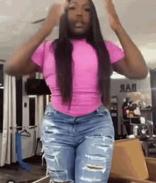 a woman wearing a pink shirt and ripped jeans is standing in a room .