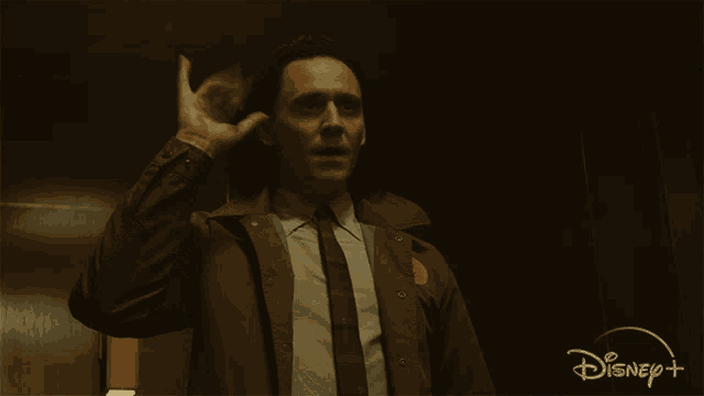 a man in a suit and tie says hi in front of a disney + logo