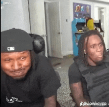 two men are sitting next to each other in a living room and looking at the camera .