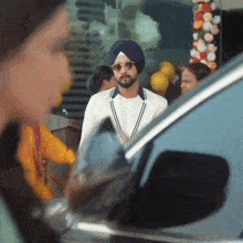 a man in a turban and sunglasses is standing in front of a car