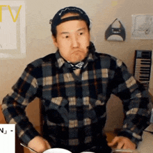 a man in a plaid shirt is playing drums and making a funny face .