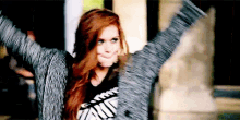 a woman with red hair is standing with her arms outstretched and making a face .