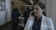 a woman in a lab coat is talking on a cell phone in a hospital hallway sponsored by global