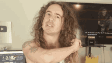 a man with long curly hair is standing in front of a tv screen that says " tv will soon turn off by its tv standby "