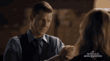 a man in a suit and tie holds a woman 's hand in front of a sign that says hallmark movies & mysteries
