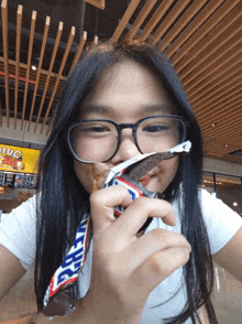 a girl with glasses is eating a snickers bar in a restaurant