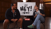 two men are sitting in front of a sign that says hey ( ew )