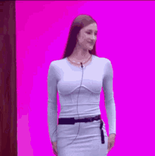 a woman in a blue dress is standing in front of a pink background and smiling .