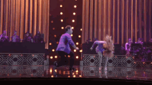 a man in a purple suit is dancing with a woman on a stage