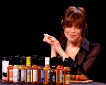 a woman is sitting at a table with bottles of hot sauce