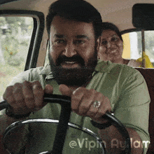 a man with a beard and a ring on his finger is driving a car with a woman in the back seat