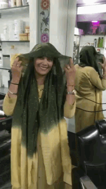 a woman wearing a green scarf is smiling in front of a mirror in a salon
