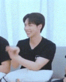 a man in a black shirt is clapping his hands while sitting on a couch with other people .