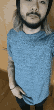 a man with long hair and a beard is wearing a blue shirt and a black helmet .
