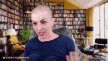 a woman with a shaved head sits in front of a bookshelf