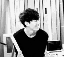 a black and white photo of a young man sitting at a table with a laptop .