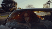 a woman with red hair is sitting in a car looking out the window