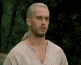 a man with white hair and a ponytail is wearing a white shirt and looking at the camera .