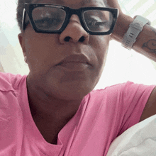 a woman wearing glasses and a pink shirt has a tattoo on her wrist