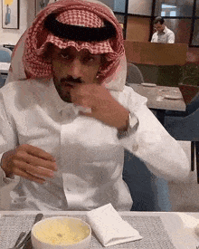 a man wearing a head scarf is sitting at a table with a bowl of food