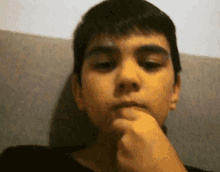 a young boy holds his hand to his chin while looking at the camera