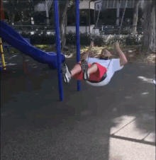 a man in red shorts is swinging on a swing set in a park .