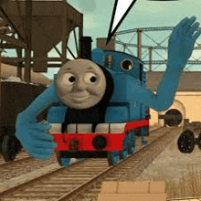 thomas the tank engine is waving at the camera while sitting on the tracks .