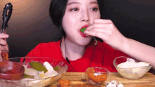 a woman in a red shirt is eating a pickle with tongs ..