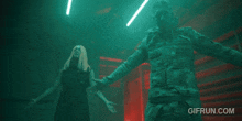 a man in a military uniform stands next to a woman with her arms outstretched in a dark room