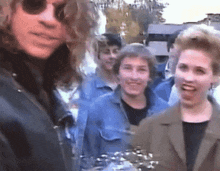 a man wearing sunglasses stands in front of a group of young people