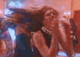 a woman in a black dress and pearl necklace is dancing in a club .
