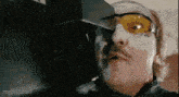 a man with a mustache is wearing a pair of yellow sunglasses .