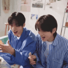 two young men in blue striped shirts are sitting next to each other looking at a cell phone .