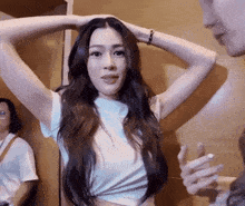 a woman in a white t-shirt is holding her hair in her hands while talking to a man .