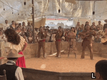 a group of people are dancing and playing instruments in front of a crowd with the letter l on the bottom right