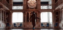 a woman in a mask is dancing in a large room with a chandelier