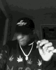 a man wearing a hat and a necklace is holding a cigarette in his hand .