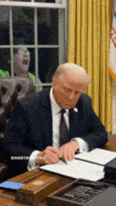 a man in a suit and tie is sitting at a desk signing a document