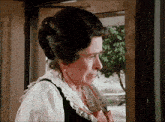 a woman in a white shirt and black vest is looking out of a window