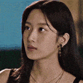 a close up of a woman 's face wearing a black tank top and earrings .