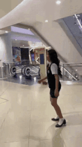 a woman in a black dress is standing in front of an escalator in a mall