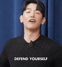 a man is wearing a black sweater and a microphone and says defend yourself