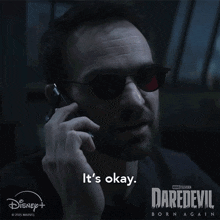 a man talking on a cell phone with a daredevil born again advertisement behind him