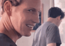a man is smiling and looking at the camera while another man stands behind him .