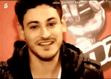 a man is smiling in front of a microphone with the number 5 on the bottom left