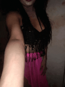 a woman is taking a selfie in a dark room while wearing a black top and pink skirt .